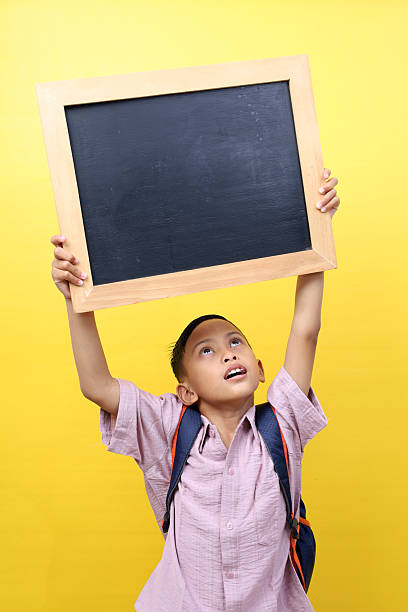 istock Happy asian schoolboy standing while showing a blank blackboard. Isolated on yellow background 2213286420