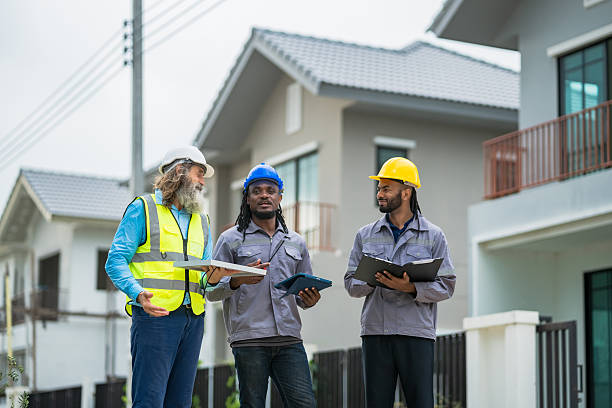 istock Three construction workers are standing outside a house, discussing plans for the project. Scene is professional and focused, as the workers are wearing safety gear and carrying blueprints 2213287897