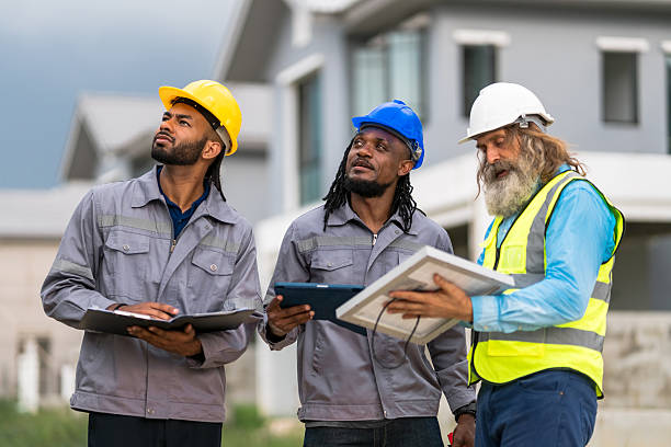 istock Three construction workers are standing together, each holding a clipboard. They are wearing hard hats and safety vests, and they appear to be discussing something related to their work 2213287911