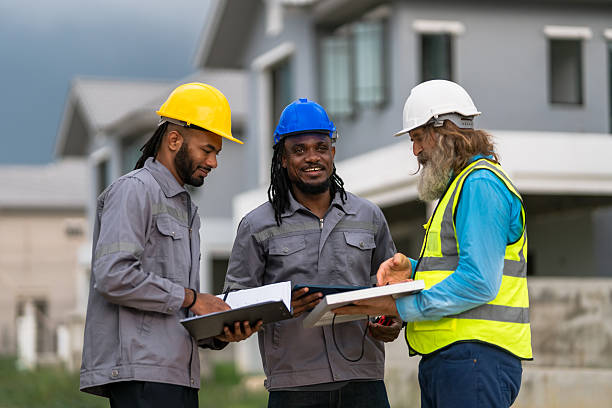 istock Three construction workers are standing together, discussing plans for a building. They are wearing hard hats and safety gear, indicating that they are working on a potentially dangerous job site 2213287915