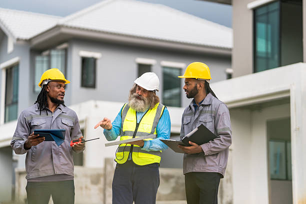istock Three men in construction gear are standing together, looking at something on their tablets. They are wearing safety vests and hard hats 2213287921