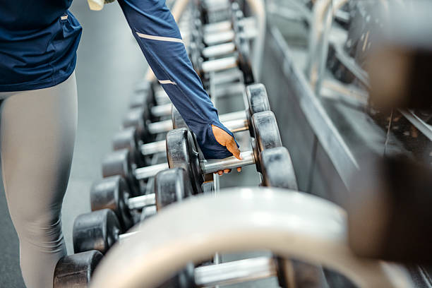 Close-up of a young woman's hand reaching for a dumbbell in a well-equipped gym, showcasing her dedication to fitness and strength training