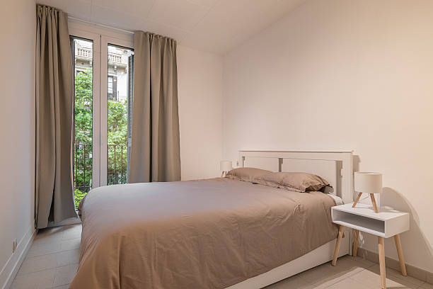 istock Simple bedroom interior with double bed, taupe bedding and large window with beige curtains 2213307143
