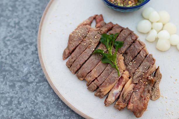 Deliciously sliced beef served with dipping sauce and garnished with herbs, ideal for culinary presentations.