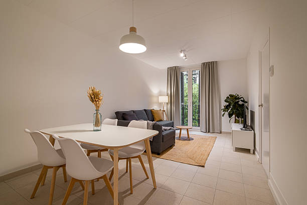 istock Minimalist dining and living area with white dining table, chairs, gray sofa, and window with natural light 2213308955