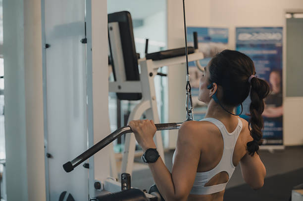 istock Powerful Back Workout Woman In White Bra Tackles Lat Pull down Machine In Bright Gym, Braid Bun, Using Gym Equipment For Sculpted Physique 2213310868