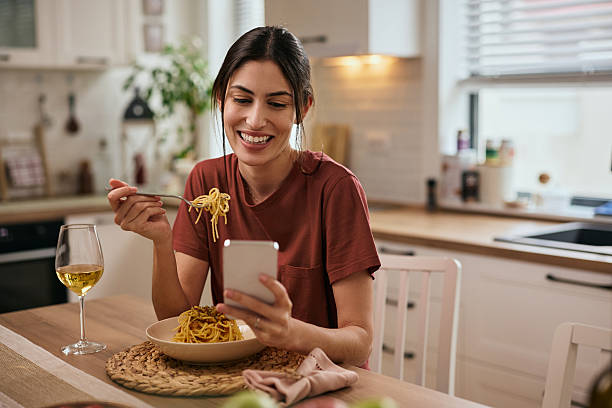 istock Happy woman eating pasta while using smart phone at dining table. 2213312477