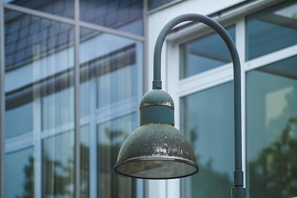 Old green streetlamp stands in front of modern glass building, showing contrast between old and new