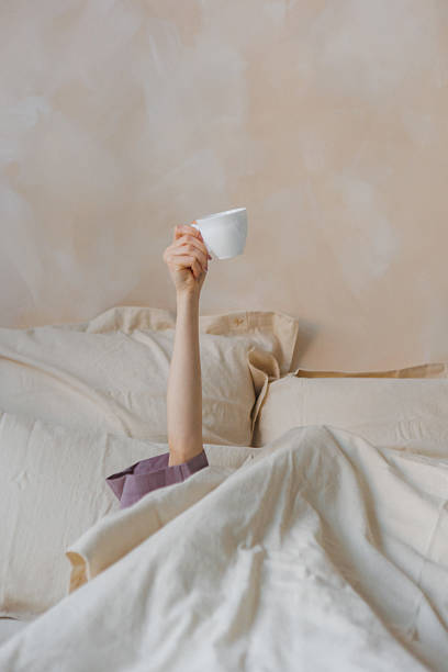 istock A person in bed holding a coffee cup above their head 2213319097