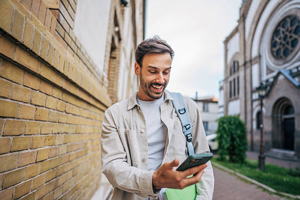 istock Smiling student walking and using phone near university building 2213320779