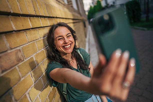 istock Young woman taking a selfie while leaning against a brick wall 2213320824