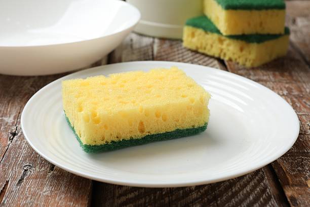 istock Yellow sponges and dishware on wooden table, closeup 2213323869