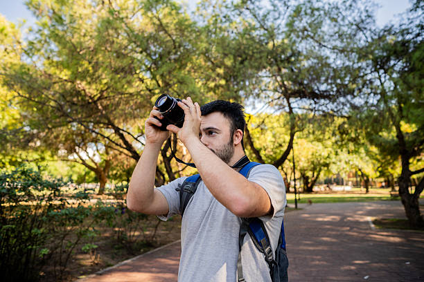 Young caucasian man student smiling and using smartphone to talk or take photos and self portrait in the city during the day