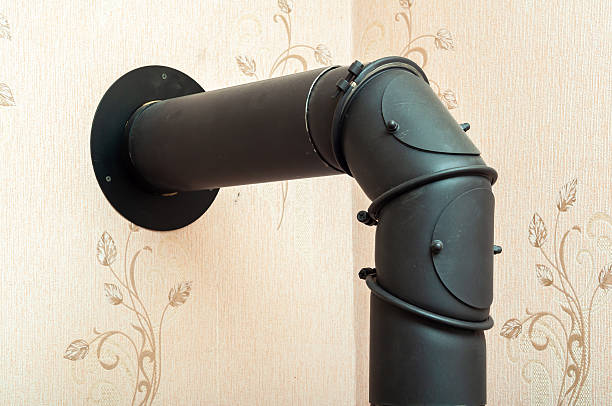 istock A black metal stove pipe angles against a beige floral patterned wallpaper, connecting to a flue. 2213331321