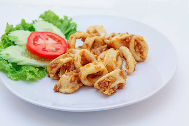 Fried stir squid with pepper and garlic, Stir-Fried Squid with Garlic, Stir-fried squid rings with crispy garlic on a white plate, served with fresh tomato and lettuce, Thai seafood