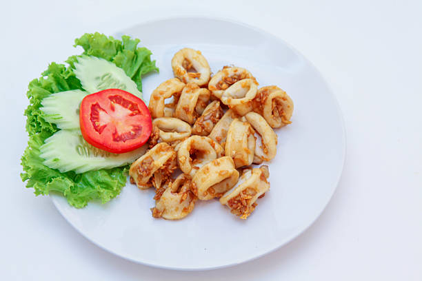 Fried stir squid with pepper and garlic, Stir-Fried Squid with Garlic, Stir-fried squid rings with crispy garlic on a white plate, served with fresh tomato and lettuce, Thai seafood