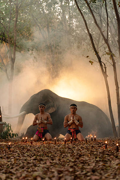 Muay Thai fighters performing a traditional wai khru ritual surrounded by candles, with a majestic elephant and glowing smoke in the background