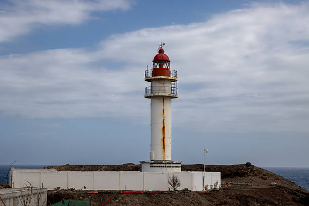 Lighthouse with white facade and red top, traditional style. Blue sky with intense clouds. Coast of Atlantic ocean. Taliarte, Las Palmas, Gran Canaria, Canary Islands, Spain.