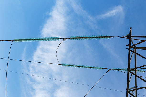 Bright blue sky serves as a backdrop for electrical insulators on transmission lines in a rural area, ensuring safe energy transport.