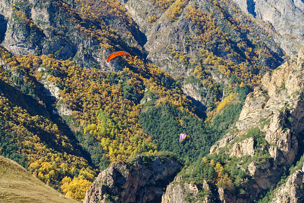 The image shows a peaceful landscape, likely Fethiye’s Ölüdeniz. A paraglider soars in the hazy sky. Below, layered green hills surround a calm body of water. The scene reflects Ölüdeniz’s serene beauty and adventurous spirit.