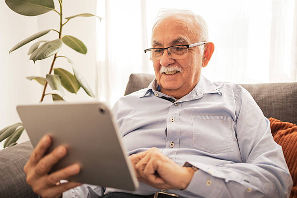istock Senior man smiling while using a tablet on a cozy living room sofa 2213343474