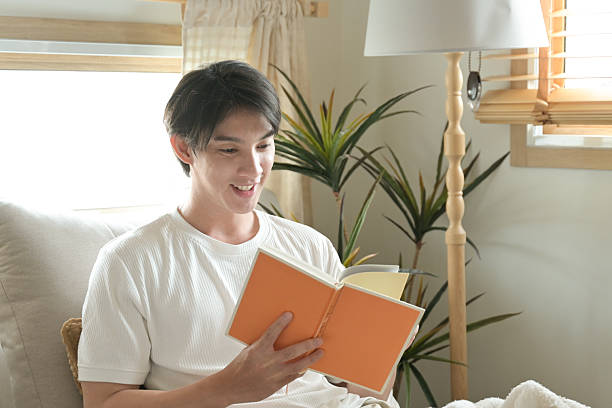 istock A man is reading a book on a couch. He is smiling and he is enjoying his time. 2213351010
