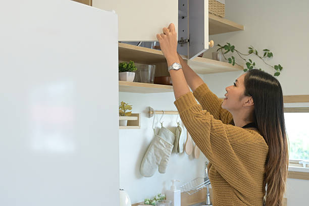 istock A woman is in a kitchen, reaching for something in a cabinet. 2213357143