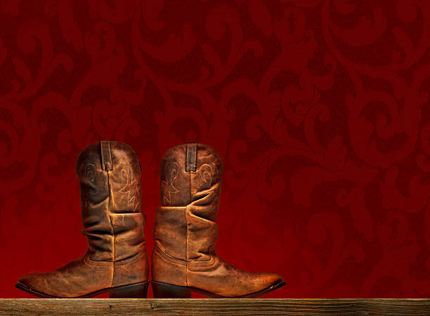 A pair of red leather cowboy boots are being worn by a woman with bare legs and standing on a light colored wooden dance floor.