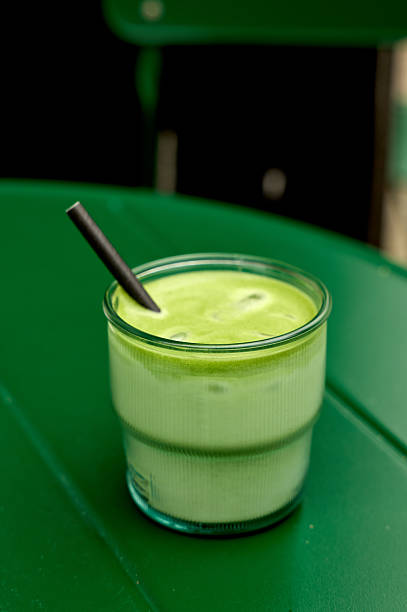 Refreshing iced matcha latte in a glass with a black straw, placed on a vibrant green table, perfect for a summer day