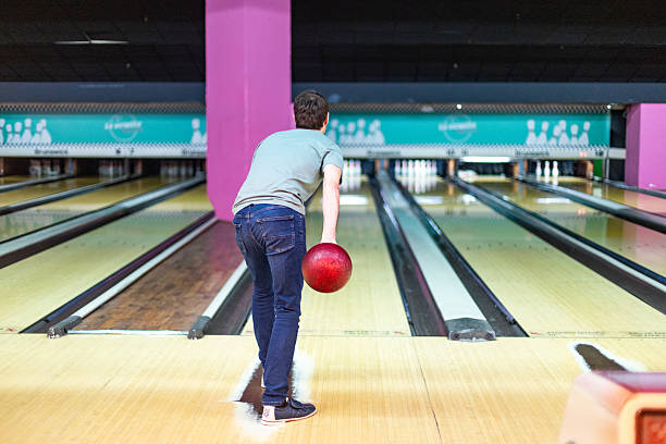 istock Young man throwing bowling ball in modern bowling alley 2213379968
