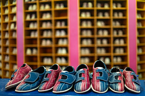 Red and blue bowling shoes sitting on a bench with blurred shoe rack in the background, ready for a fun bowling game