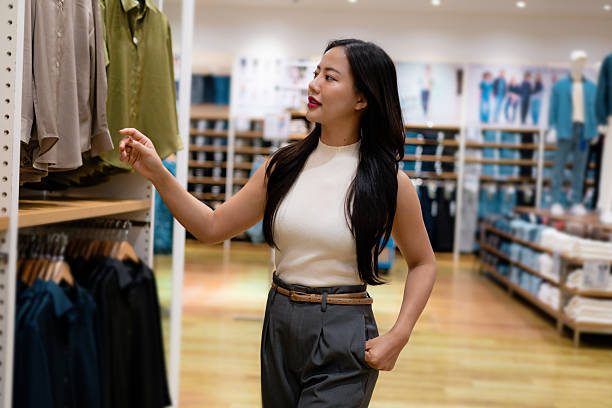 istock Elegant Asian customer browsing through a modern clothing store, thoughtfully selecting stylish garments while enjoying a satisfying shopping experience 2213383332