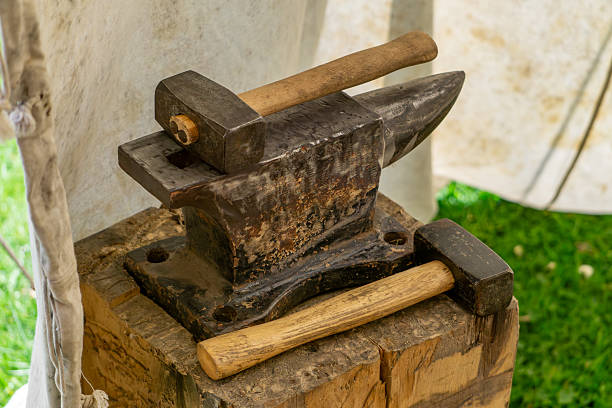 Close-up of unrecognizable person blacksmith bending wrought iron while hitting metal with hammer on anvil