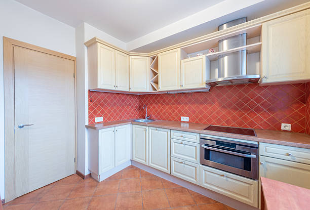 Bright and clean kitchen featuring light wooden cabinets, red tiled splashback, stainless steel fixtures, and a sleek stove design