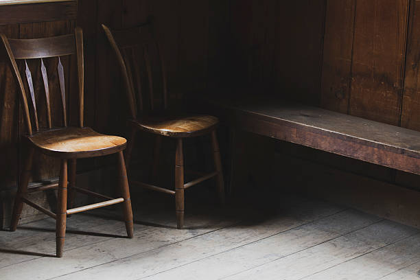Two antique wooden chairs and old bench in cozy rustic interior with soft light.