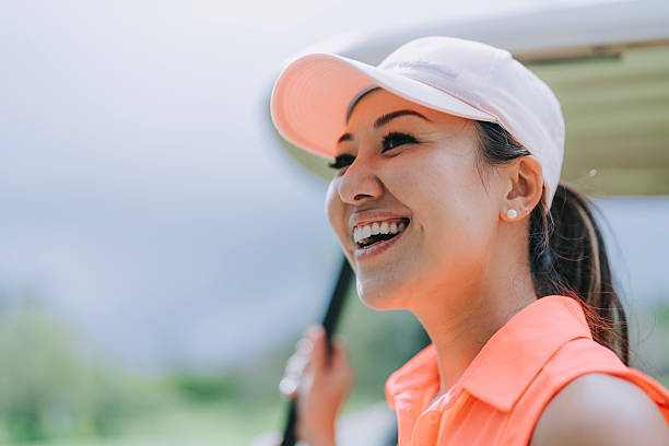 A woman is swinging a golf club. She is wearing a blue shirt and white pants. The woman is smiling as she swings the club