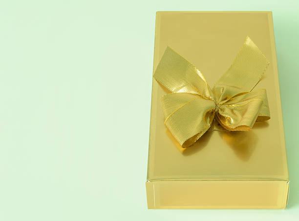 istock A gold box with a bow on top of it on a soft green background 2213421421
