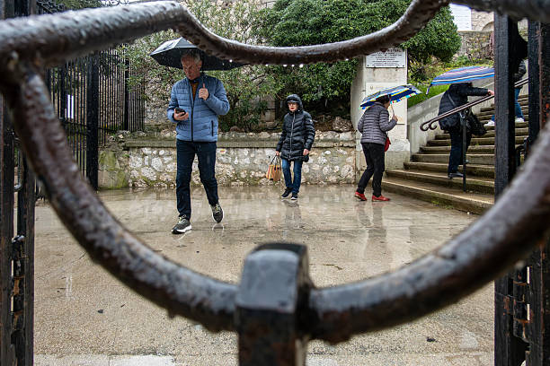 Marseille, France March 14, 2025 Pedestrians in the rain with umbrellas visit the Notre-Dame de la Garde Basilica.