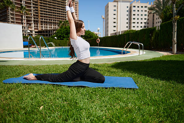 istock Woman Practicing Yoga Outdoors on Mat by Poolside in Urban Environment 2213428659