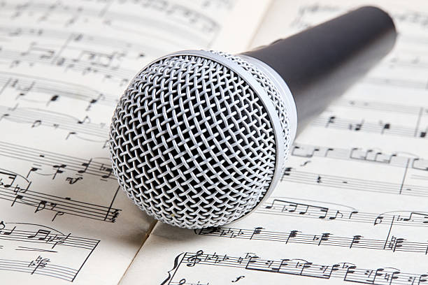 Microphone for vocal with silver metal head close up over music sheet background.