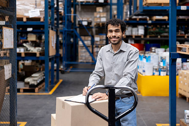 istock Foreperson working at a warehouse moving boxes with a pallet jack and taking inventory 2213436474