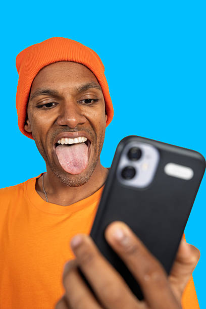 istock Playful young man sticking out tongue while using smartphone 2213455564
