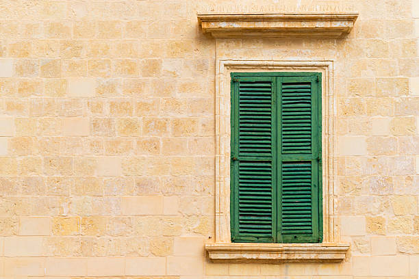 Stone brick wall with a closed green wooden window with shutters.