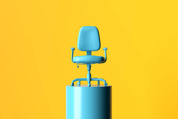 Minimalist composition featuring a blue office chair placed on a blue cylindrical pedestal against a vibrant yellow backdrop