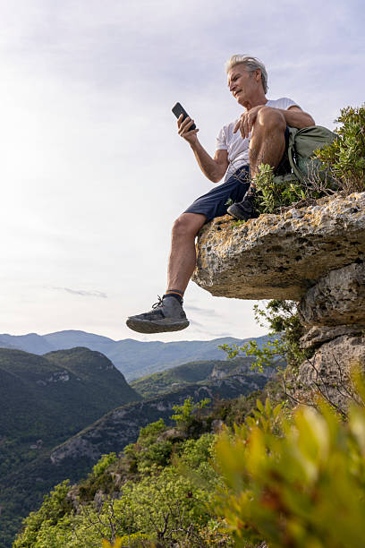 istock Mature man sits on cliff edge and uses mobile phone 2213461035