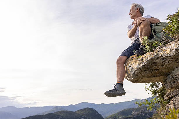 istock Mature man sits on cliff edge above mountains 2213462100