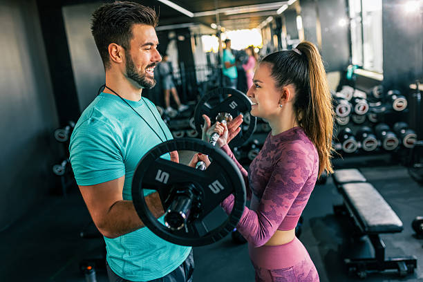 istock Young woman does shoulder press with weights in the gym while her personal trainer is spotting her. 2213462887