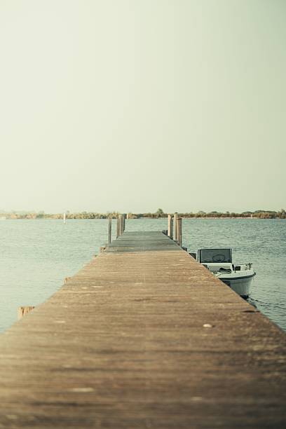 A serene wooden pier extending into calm waters with a small boat moored beside it under a clear sky.