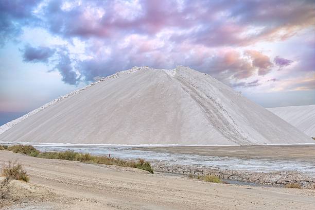 A massive, pristine white mound of salt dominates the landscape under a dramatic sky, Aigues-Mortes, France.