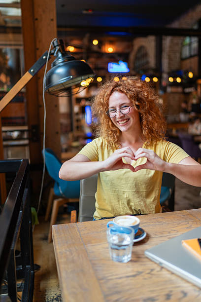 istock Smiling freelancer woman making heart shape with hands in cafe 2213469700